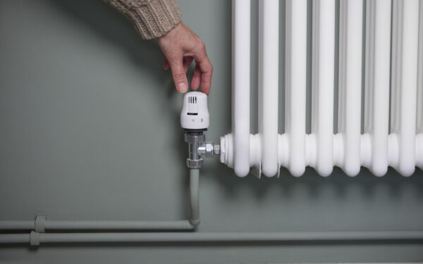 Close Up Of Hand Turning Down Thermostat On Radiator At Home To Save Energy And Money