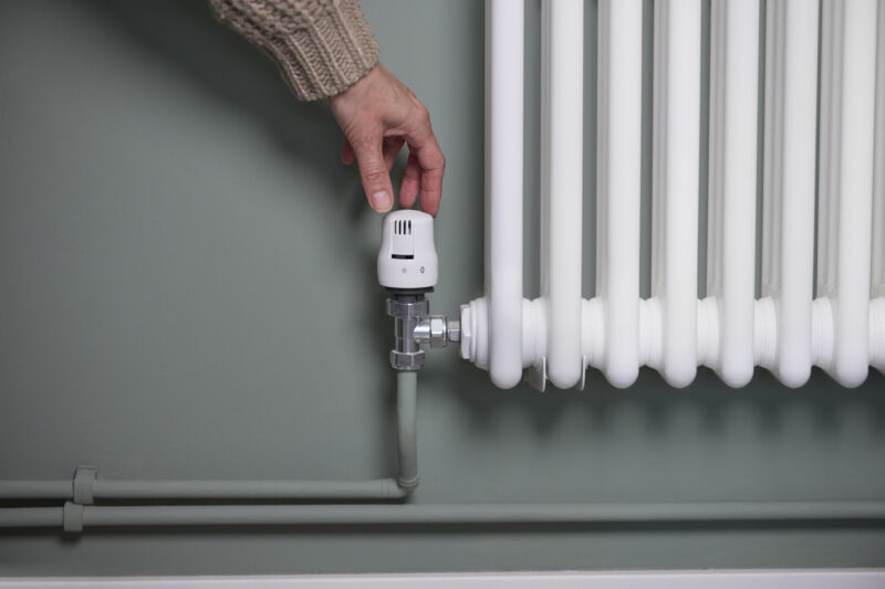 Close Up Of Hand Turning Down Thermostat On Radiator At Home To Save Energy And Money
