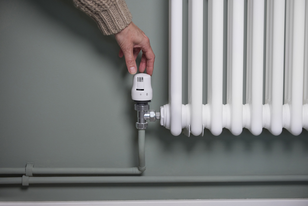 Close Up Of Hand Turning Down Thermostat On Radiator At Home To Save Energy And Money