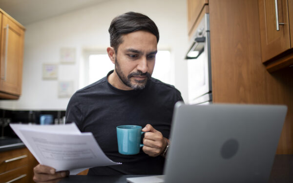 Mid adult male checking his personal finances on a laptop computer in the kitchen at home