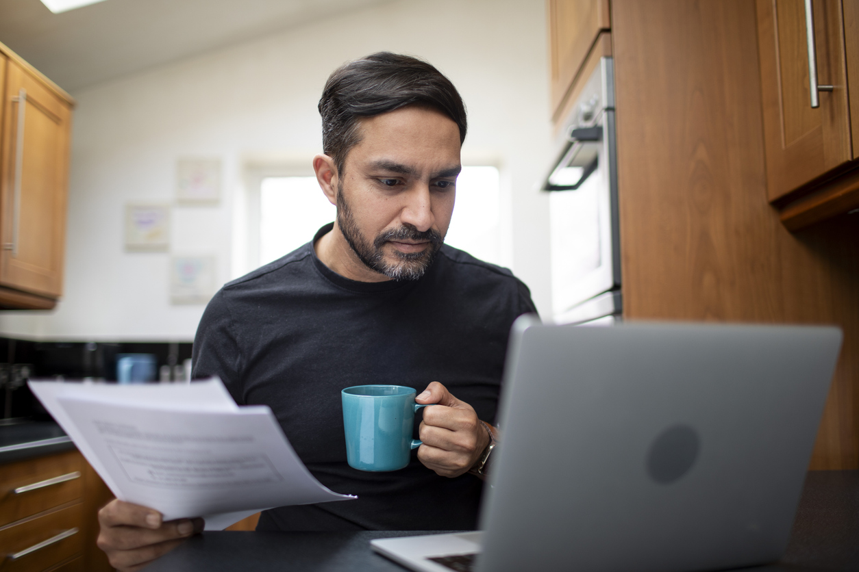 Mid adult male checking his personal finances on a laptop computer in the kitchen at home
